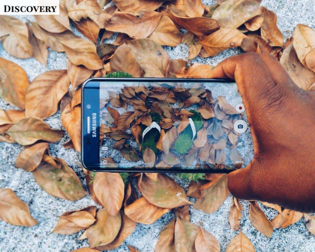 black Samsung Galaxy smartphone taking photo of green flip flops with dried leaves