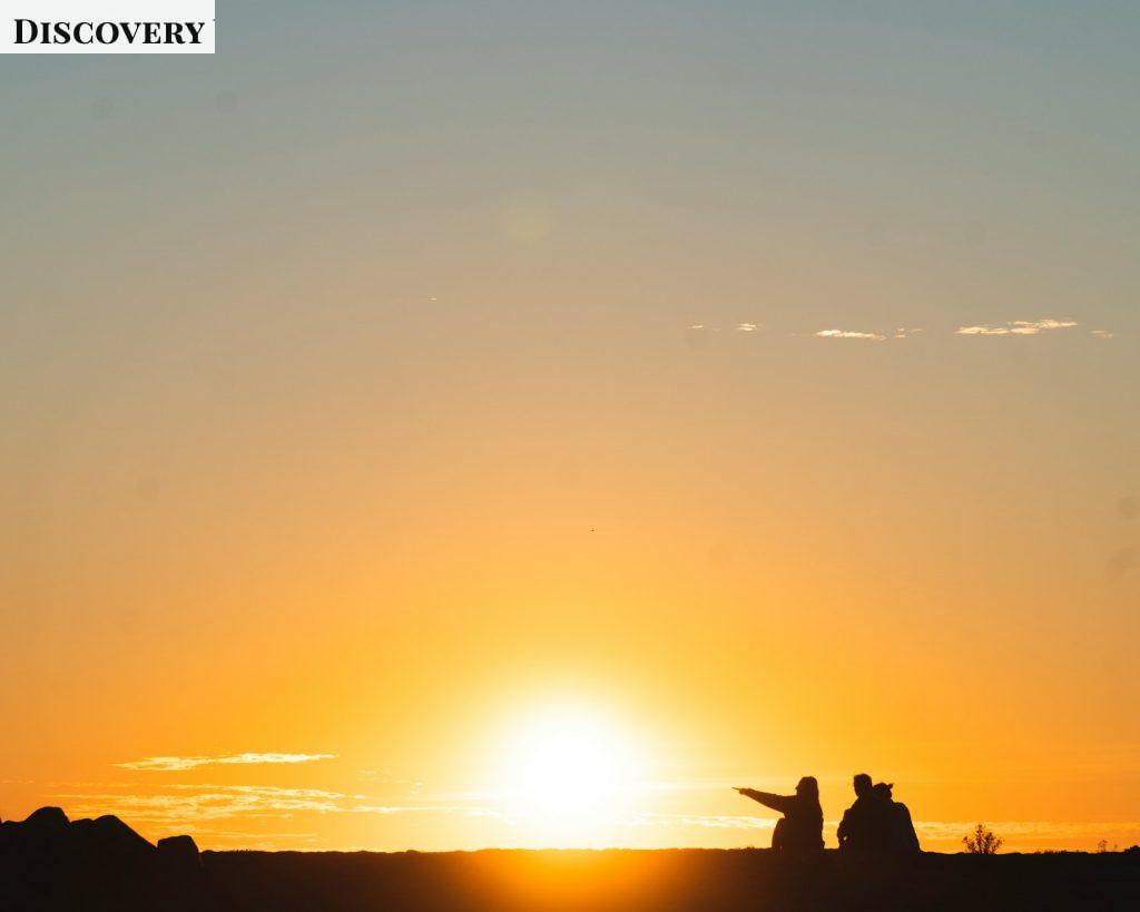 silhouette of three people sitting on land during golden hour